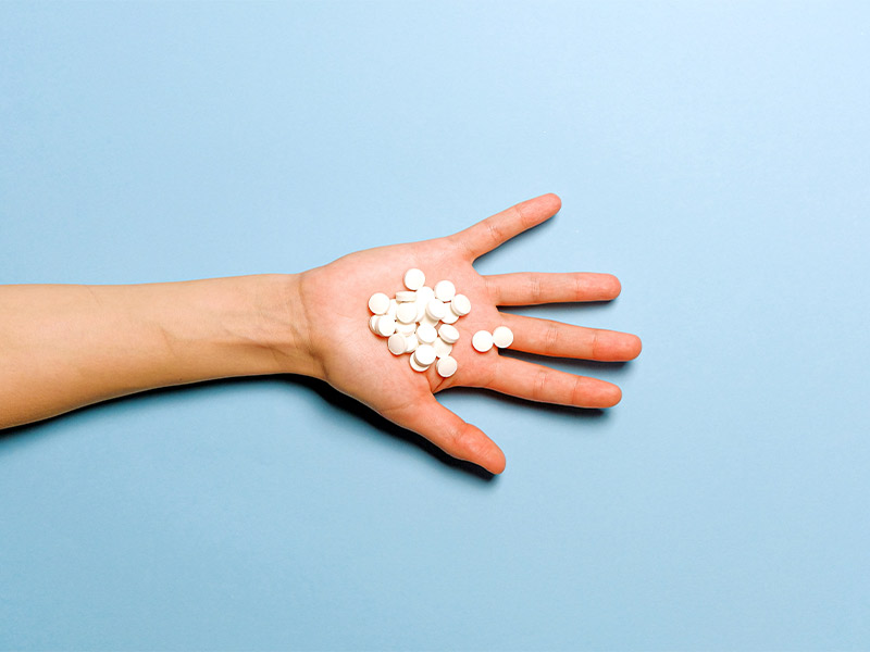 hand on a blue background holding opioid pills