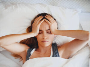woman laying in bed holding her head suffering from adderall side effects
