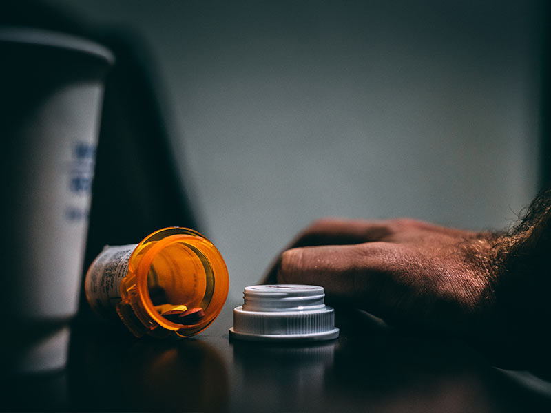 pill bottle on a table next to a cup showing an example of a relapse trigger